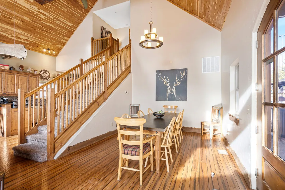 A bright, welcoming dining area featuring a large table ideal for family dinners or group celebrations, a staircase adding architectural interest, and wall art contributing to a homey atmosphere. The setting is designed for social gatherings and memorable shared meals.