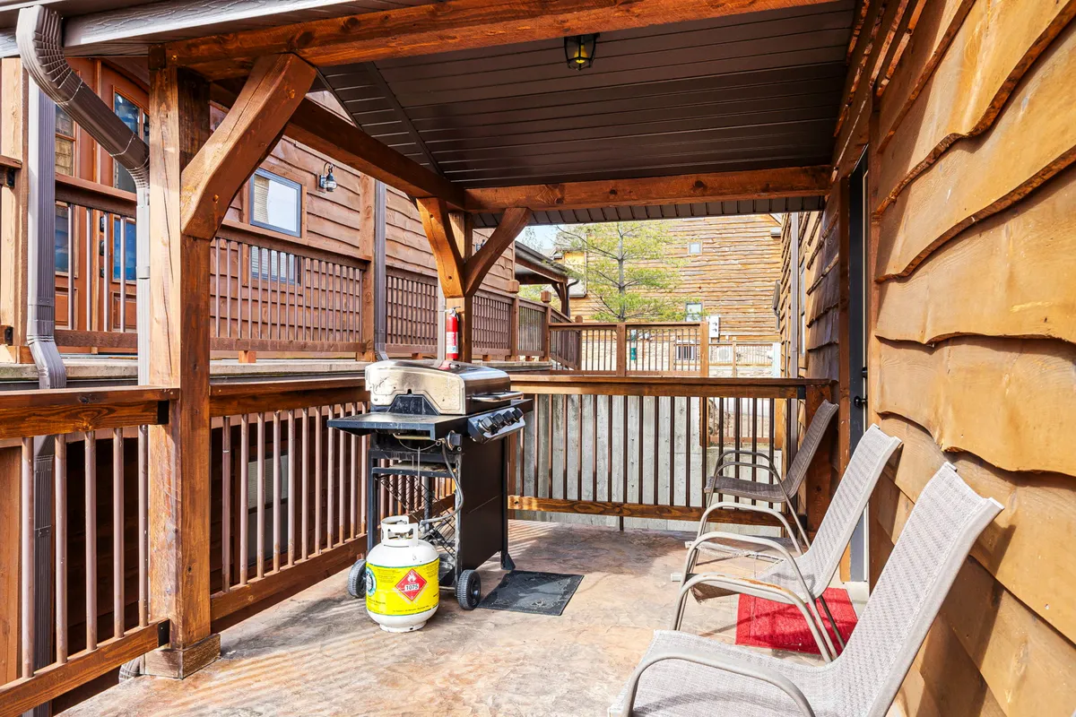 A close-up of a grill and a cozy seating area set on a wooden patio, with surrounding greenery adding to the relaxed, outdoor ambiance. The grill takes center stage, equipped for family barbecues or al fresco dinners, while the seating area invites quiet conversation or group gatherings.