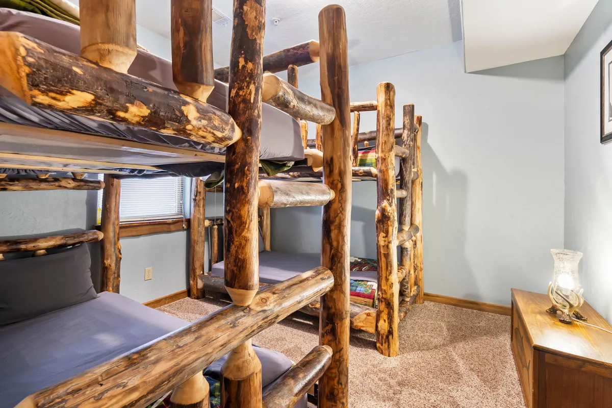 A cozy bunk room featuring rustic log bunk beds, a wooden nightstand, and soft lamps. The playful and inviting setup is perfect for children or cousins, offering a space for late-night conversations and group fun.