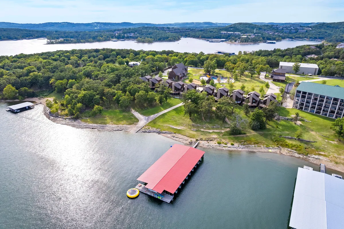 A peaceful lakeside scene featuring a dock with a red roof, surrounded by lush green trees and waterfront cabins. The calm waters invite outdoor activities and showcase how easily accessible the lake is from the property.