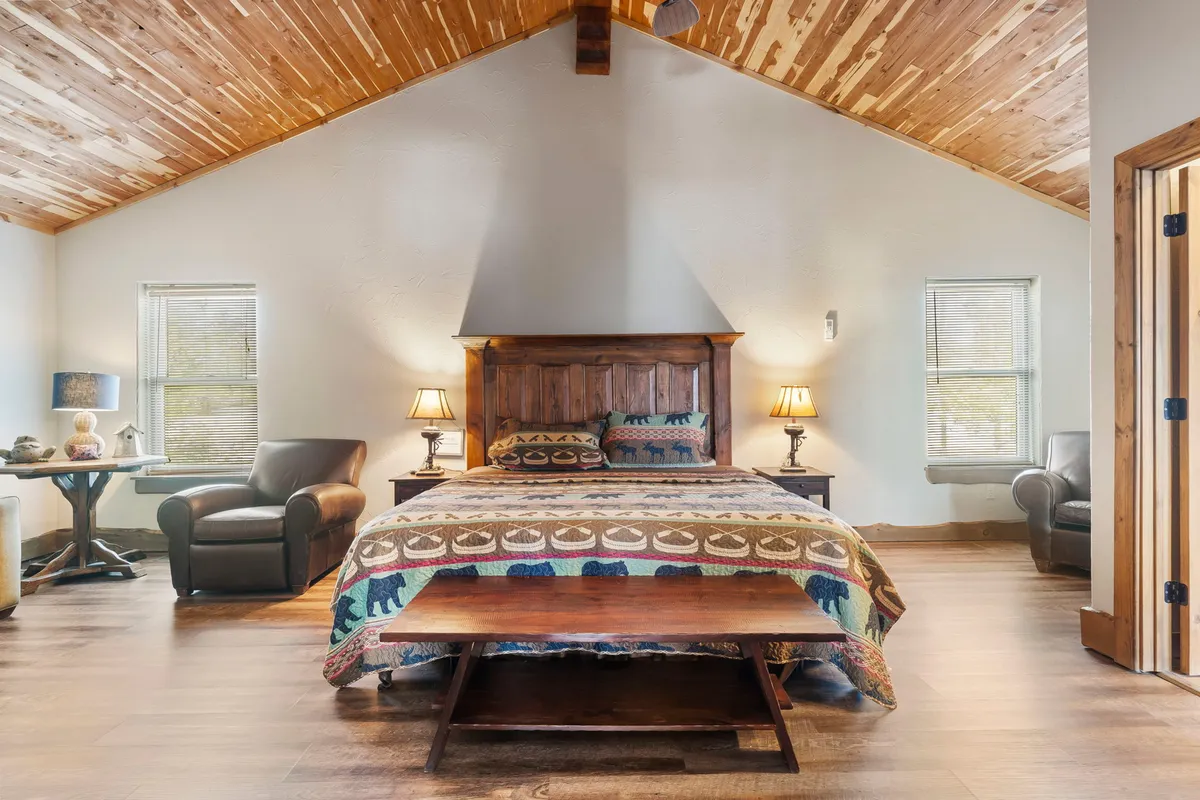 A king-sized wooden bed with a colorful quilt is the focal point of a spacious bedroom. Accent chairs sit nearby, along with side tables and lamps, creating a relaxing atmosphere suitable for parents, grandparents, or couples seeking comfort and privacy.