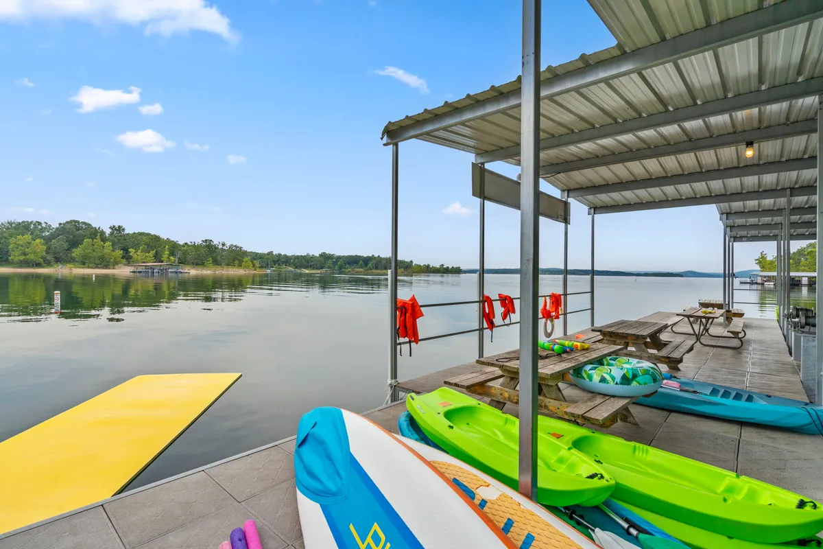 A lively setup showing kayaks on a floating dock, picnic tables ready for gatherings, life jackets for safety, and expansive views of the lake. The surrounding natural beauty and recreational equipment emphasize outdoor activity and togetherness.