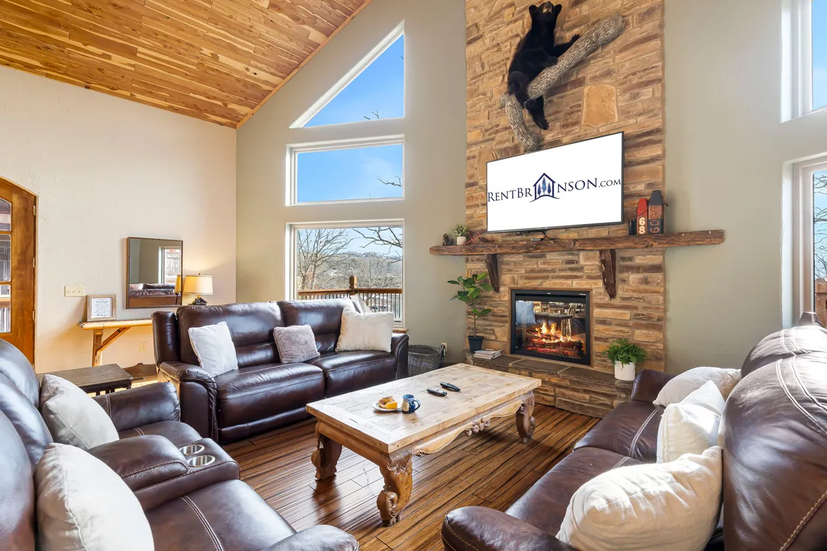 This cozy living area showcases a substantial stone fireplace, plush leather sofas, a wooden coffee table for board games or snacks, and a TV mounted on the wall. The space is warm and welcoming, ideal for relaxing after games or gathering together for a movie or family game night.