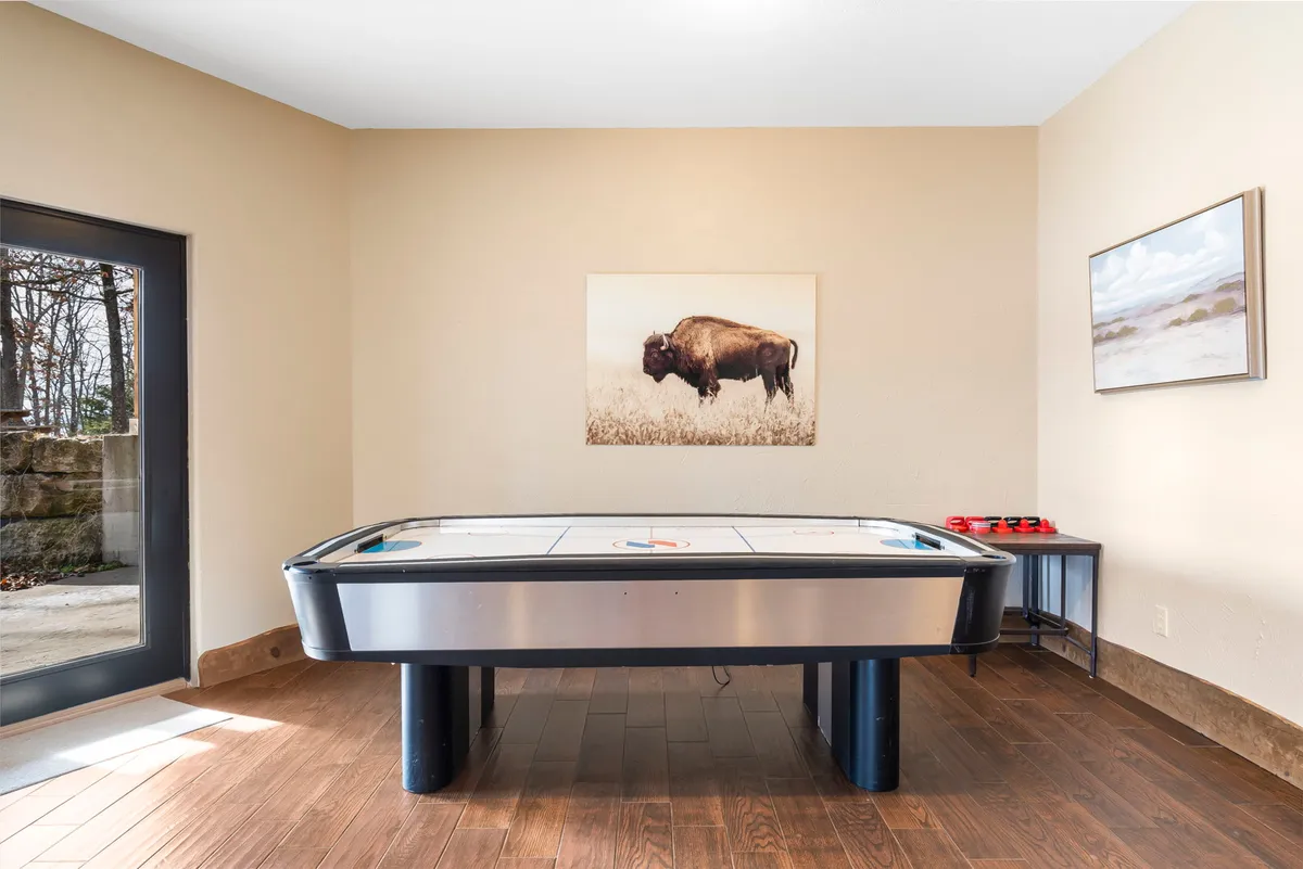 This image features a dedicated game area in the lower-level living space, complete with an air hockey table as its focal point, vibrant bison artwork on the wall, and a large window letting in natural light. The room is designed for energetic activities and encourages social interaction, perfectly matching the 'Fun & Games Retreat' theme.