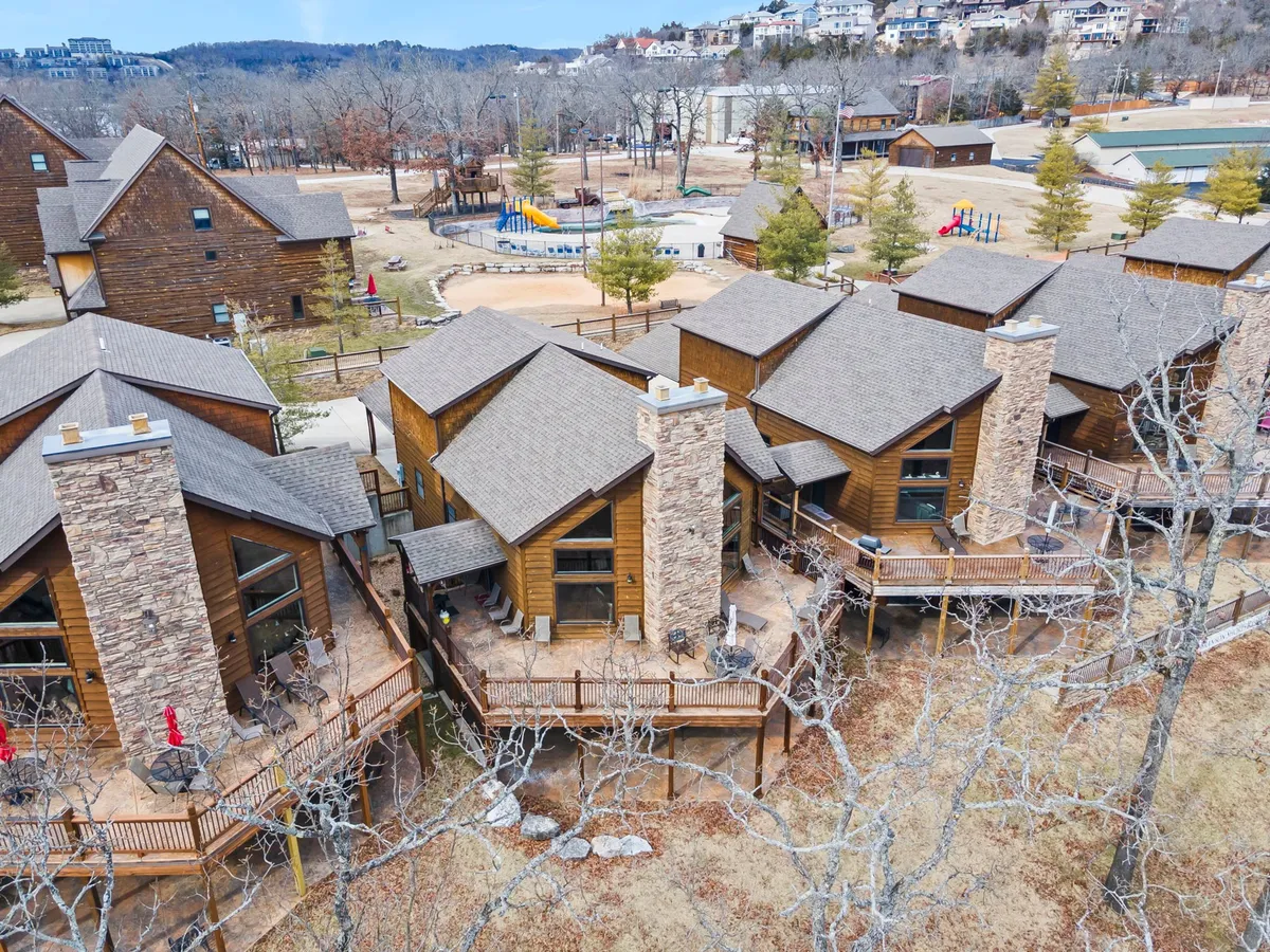 A welcoming view of wooden cabins with stone chimneys and decking areas, plus a playground in the background. The communal deck spaces and open surroundings offer plenty of room for relaxing or playing outdoors.