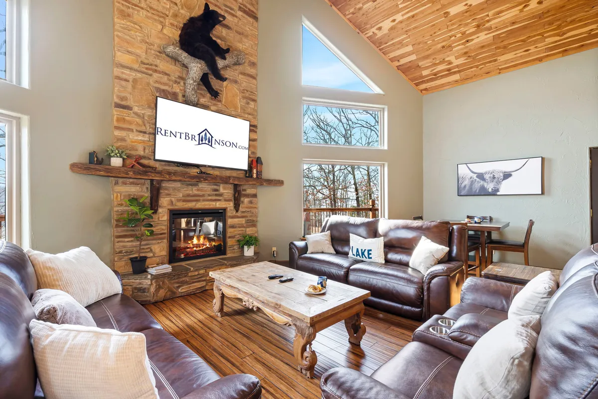 This inviting interior captures a similar lower-level vibe, with a large stone fireplace, bear-themed decor, plush sofas, and big windows offering nature views. The space looks perfect for both quiet relaxation and group activities, such as family game nights mentioned in the section.